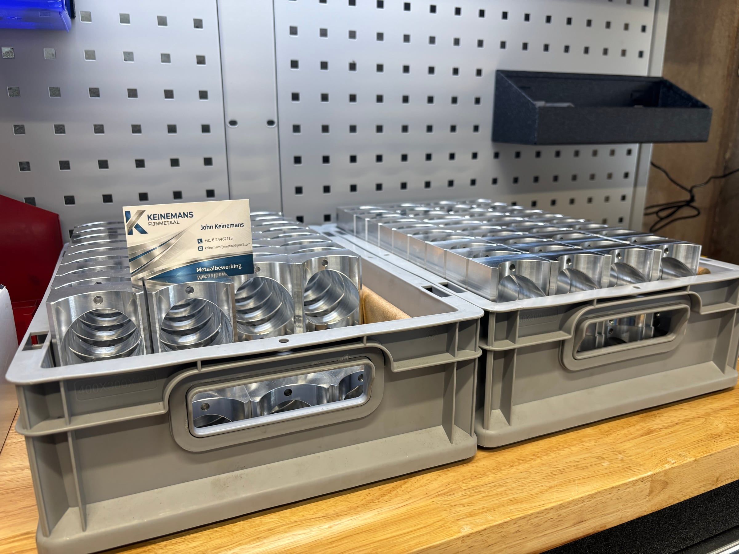 Twee kratten vol gefreesde aluminium onderdelen, met het visitekaartje van Keinemans Fijnmetaal.